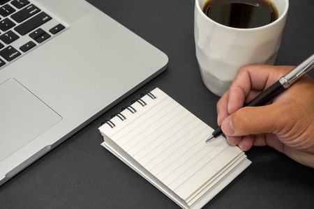 Hand holding a pen and writing on notebook. Text copy space.の写真素材