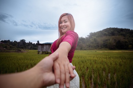 Woman turning and smiling while holding your hand in paddy field.の写真素材