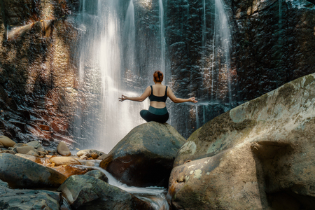 Woman doing yoga pose in front of a waterfall at Kionsom Park, Sabah, Malaysia.の写真素材