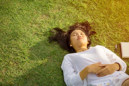 Asian teenage girl lying down on grass in the park and enjoying the moment of peace.の写真素材