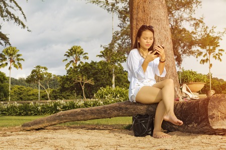 Asian teenage girl sitting crossed legs and looking at her phone.の写真素材