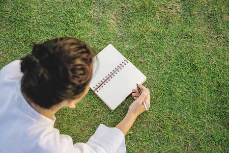 Woman writing on a notebook in a public park with field grass. Back view face downwards.の写真素材