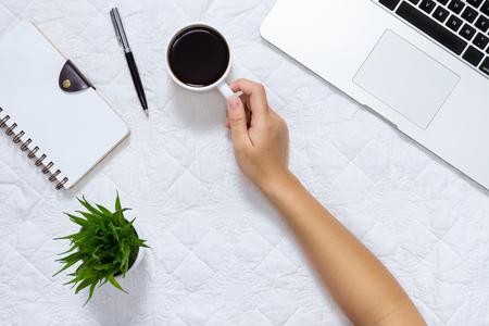 Woman hand holding coffee cup on table with laptop and spiral notebook.の写真素材