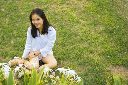 Happy smiling young Asian teenage girl sitting on grass in the park.の写真素材