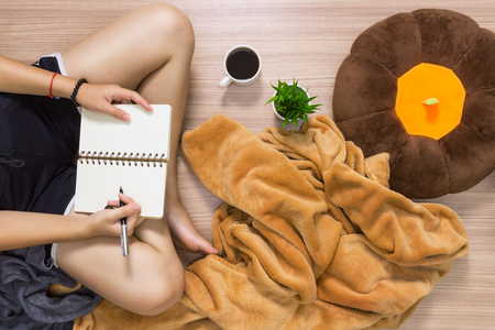 Woman sitting with legs crossed on wooden surface while writing on spiral notebook. Domestic life lifestyle concept.の写真素材