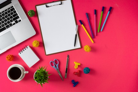 Office supply items, laptop and coffee on pink background. Colorful and vibrant office table still...