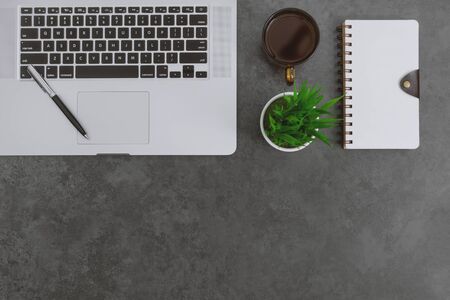 Overhead view of work desk with laptop, notebook, pen and potted plant on dark gray background.の写真素材