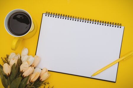 Overhead View of Notepad and Coffee Cup with Flower on Yellow Backgroundの写真素材