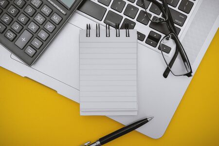 Overhead View of Notepad, Calculator and Laptop over Yellow Background.の写真素材