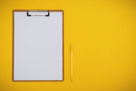 Overhead View of Paper on Clipboard and Pen on Yellow Background