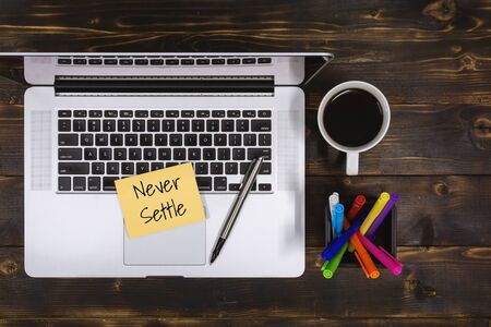 Never Settle. Overhead view of Sticky Note and Laptop on Rustic Wood.の写真素材