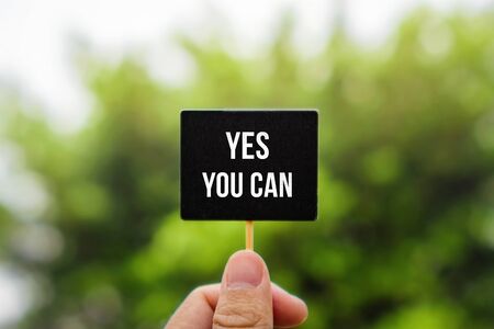 Motivational and Inspirational Quote. Yes You Can. Hand Holding Stick Blackboard Against Green Nature.の写真素材