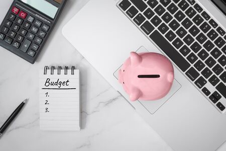 Budget Written on Notebook and Piggy Bank on Laptop.