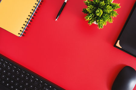 "Red Desk with Essential Tools" - A red flat lay desk with a pen, keyboard, mouse, planner, and potted plant for a productive workspace.の写真素材
