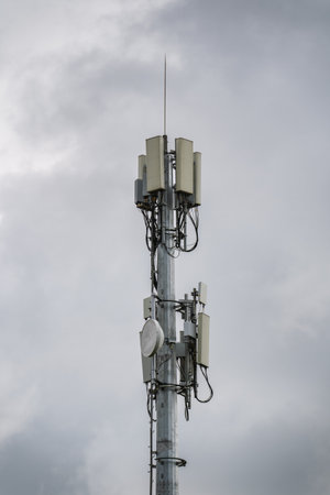 Cell phone tower with multiple antennas against a cloudy sky.