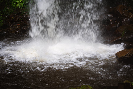 Close-up photo of waterfall splashing on rocks in lush forest setting.の写真素材