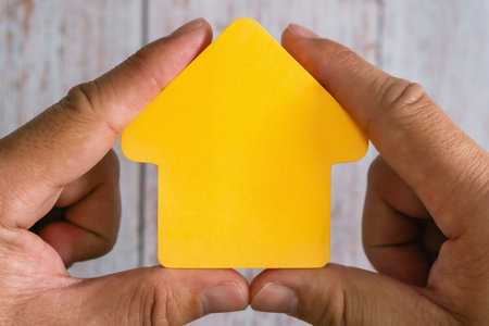 Conceptual image featuring hands holding yellow home shape - representing property ownership and housing market.の写真素材