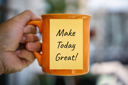 Close-up photo of an orange coffee mug with an inspirational message on a sticky note.の写真素材