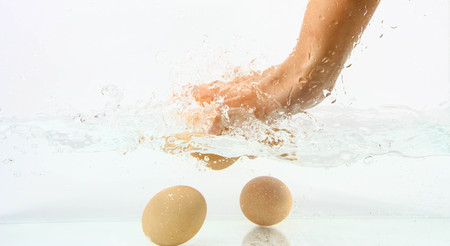 Eggs in hand into clear water splashの写真素材