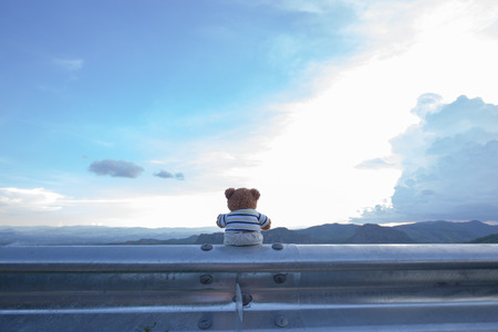Teddy bear doll sit on steel bar with landscape and cloud scapeの写真素材