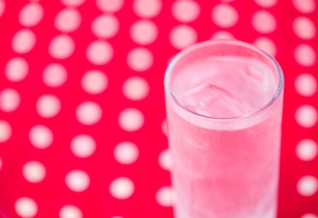 Pure water with ice in tall glass standing on red cloth and white polka dotの写真素材