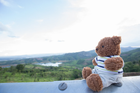 Teddy bear doll sit on steel bar with landscape and cloud scape