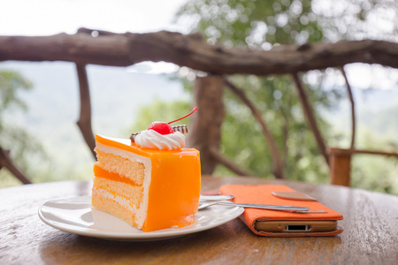 Orange piece of cake with layer and red cherry on white plate  and wooden tableの写真素材