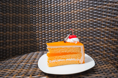 Orange piece of cake with layer and red cherry on white plate  and wooden tableの写真素材