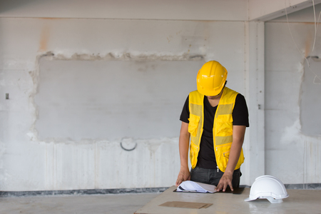 Asian male worker in yellow hard helmet and vest as for safety in underconstructed building as survey and checking projectの写真素材