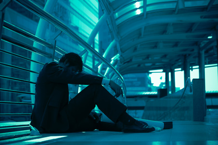 Disappointed Asian middle age businessman sitting in outside office as city backgroundの写真素材