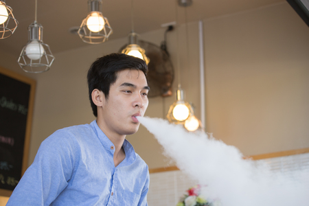 Young Asian man wearing blue T-shirt, exhale with smoke from tabacco or cigaretteの写真素材