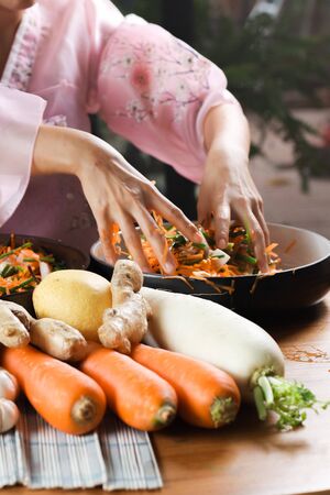 Woman in traditional dress, Hanbok, makes Kimchi,Korean cuisine famous side dish, fermented vegetables, cabbage and radish, spicy and smelly seasonings including apple or pear, onions, garlic, ginger, spring, onion and mushroom.の写真素材