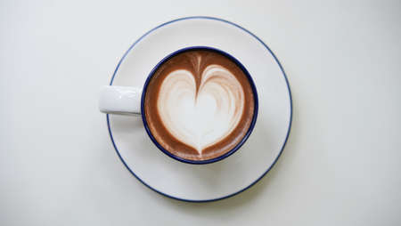 Latte art hot coffee with tulip milk latte art on top of white ceramic glass set on wood table in coffee shop Hot chocolate drink with white foam and cacao brown powder on top in transparent short cup with saucer. Beverage on table in coffee shop.の写真素材