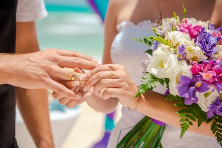 Hands and rings on wedding bouquet on the beachの写真素材