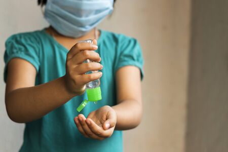 an Indian Asian girl child wearing safety nose mask sanitizing hands during novel corona virus or COVID-19 outbreak with selective focus, shallow depth of field and blurred backgroundの写真素材