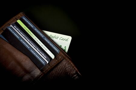 debit card peeping out from brown wallet on black background