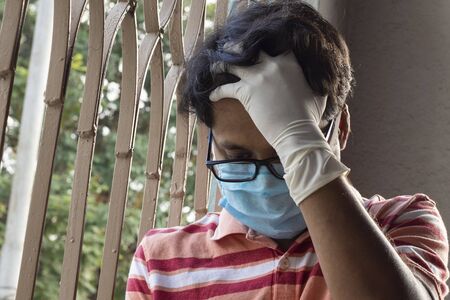 an Indian or Asian person wearing nose mask and hand gloves feeling depression after staying at home during lockdown due to COVID-19 or corona virus outbreakの写真素材