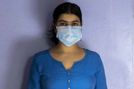 an Indian woman wearing surgical nose mask and looking at camera for corona virus or covid-19 protection on white backgroundの写真素材