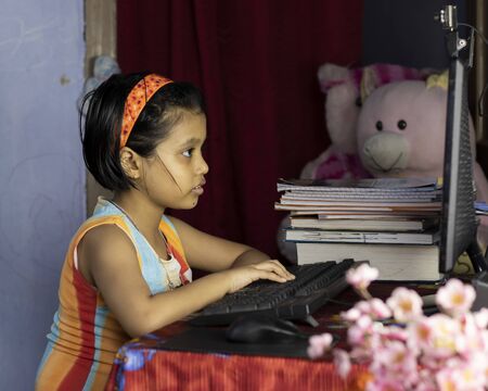 an Indian girl child with intense face attending online class on desktop computer during COVID-19...