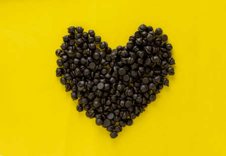 symbol of heart made with dark chocolate chips in yellow background