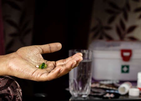 tablet and capsule on human hand with selective focus and water glass and medicines on background at...