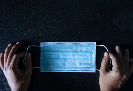 surgical mask on black grainy floor held in hand with space for text