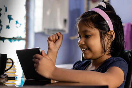an Indian cute girl child playing video games at home with tablet
