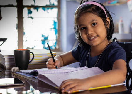 an Indian cute girl child studying at home with smiling face