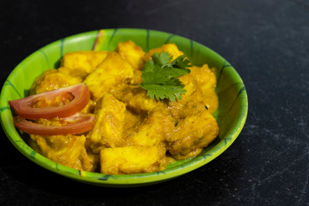 high angle view of paneer masala garnished with tomato and coriander leaves in green plate and dark backgroundの写真素材