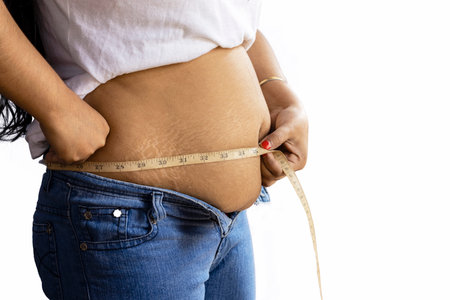 mid section side view of an Indian woman measuring fat belly with tape on white background