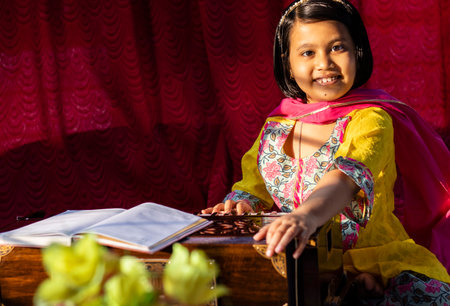 an Indian cute girl child looking at camera and playing harmonium in ethnic dress