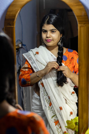 a beautiful Indian woman in white saree knotting hair in front of mirror with smiling face