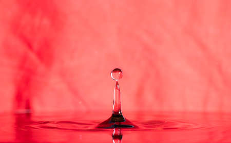 form of water droplets after falling on rippled water surface on red backgroundの写真素材