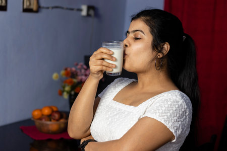 an Indian Asian woman kissing a glass of milk in a domestic roomの写真素材